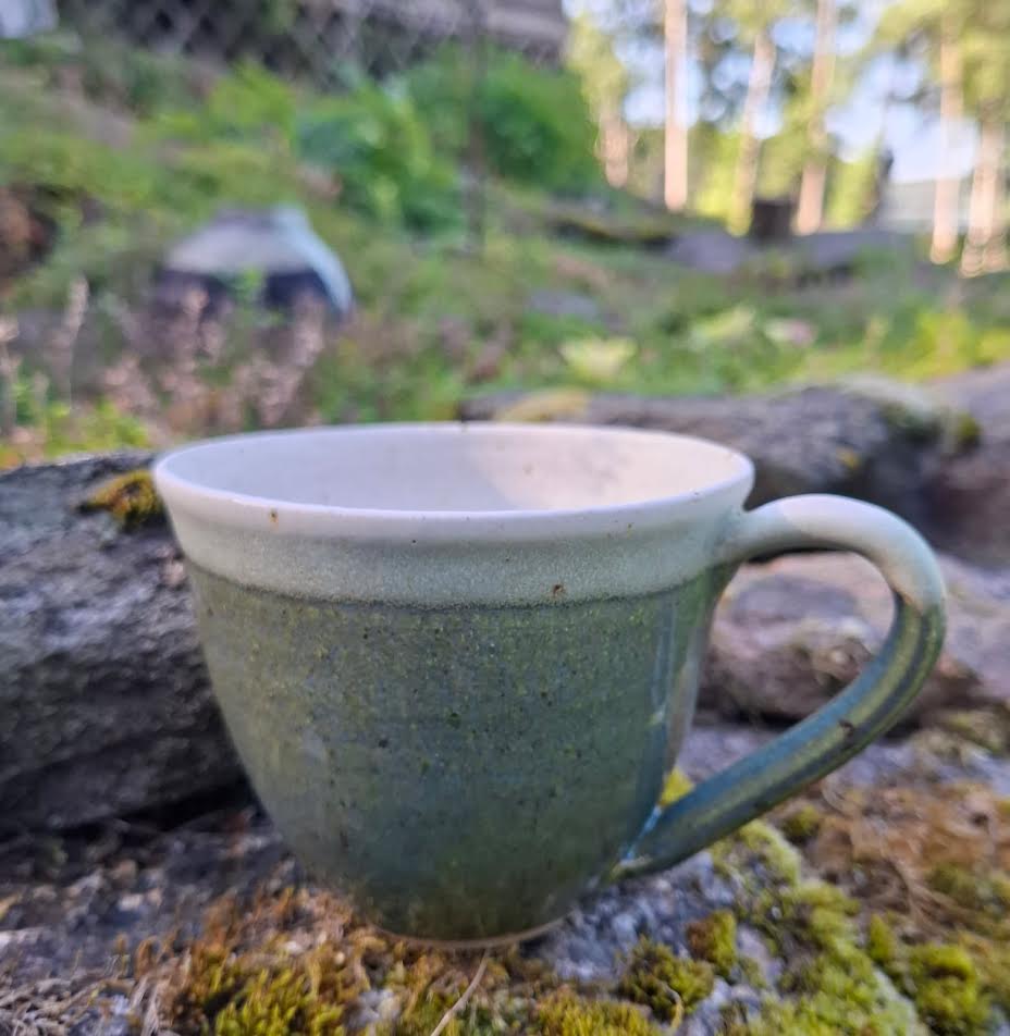 Grön mugg med vit överkant på mossig sten
