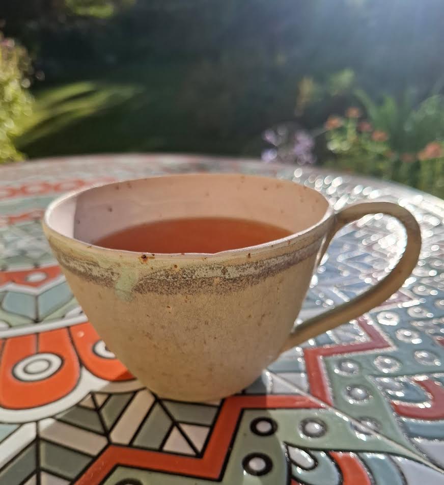 Beige kopp med te och grönbrun kantdekor
