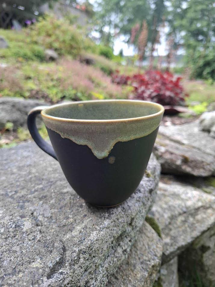 Svart kopp med grönbrun rinnande glasyr längs kanten